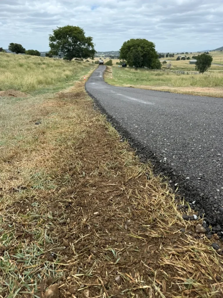 Newly paved asphalt driveway along a rural hillside