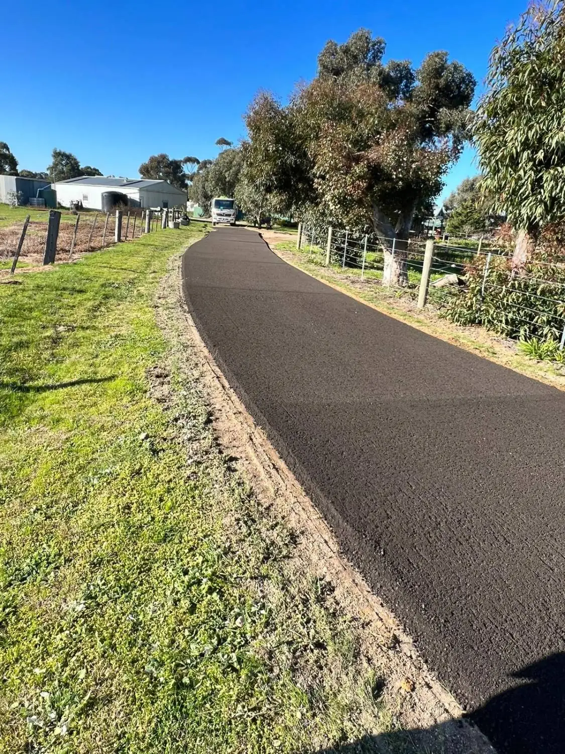 Newly paved asphalt driveway leading through a rural property