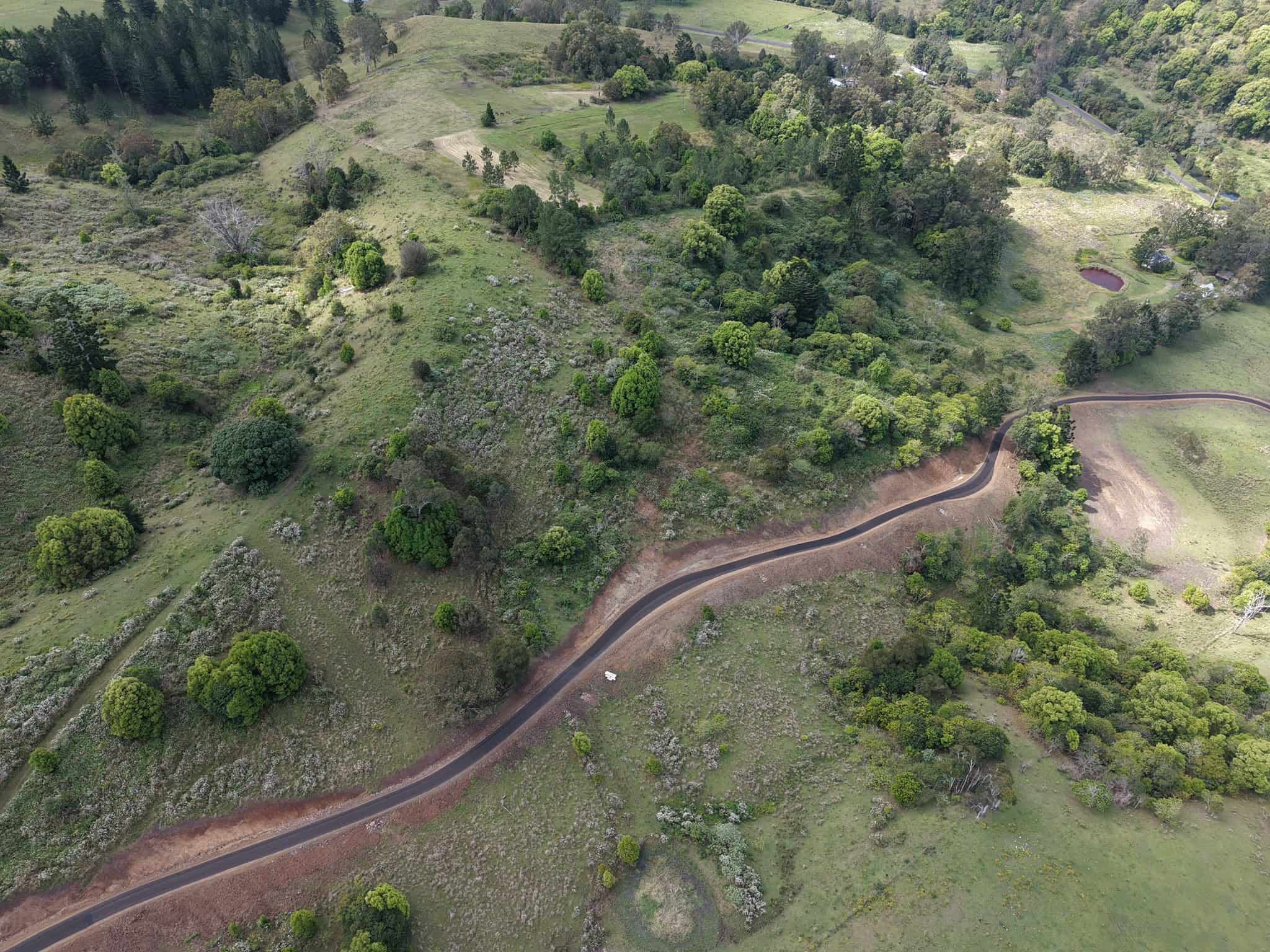Aerial view of a newly constructed paved road winding through a green rural landscape.